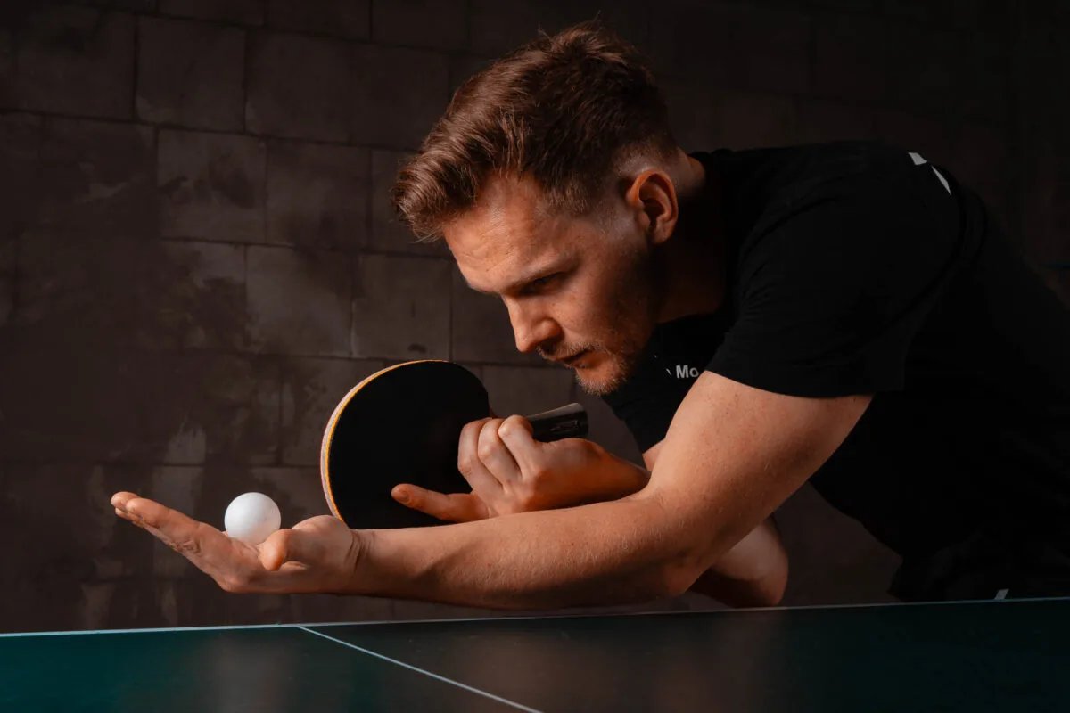 Tischtennisspieler hält Ball und Schläger vor dem Aufschlag, konzentrierter Blick nach unten